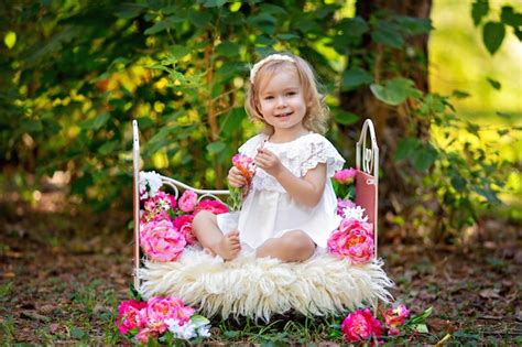 여름에 야외에서 핑크 꽃과 함께 침대에서 복고풍 공주 복장에 행복 한 어린 소녀 프리미엄 사진