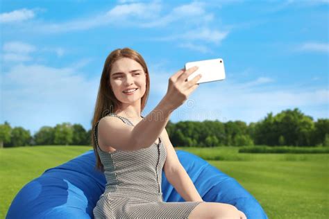 Young Woman Taking Selfie While Sitting On Bean Bag Chair Outdoors