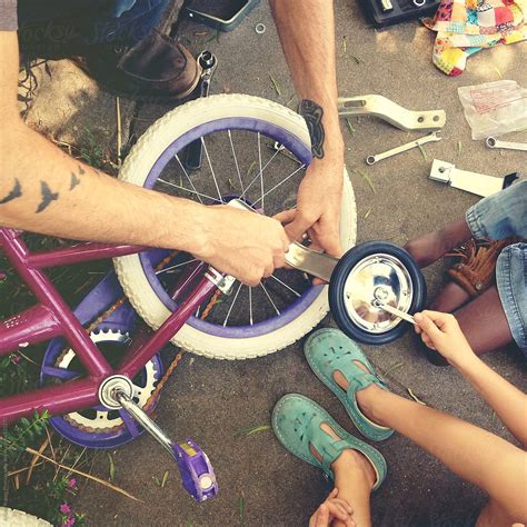 Father Putting Training Wheels On Bike With Children By Kristin Rogers
