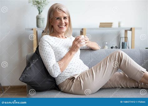 Portrait Of Smiling Mature Woman Relaxing On Couch With Cup Stock Photo