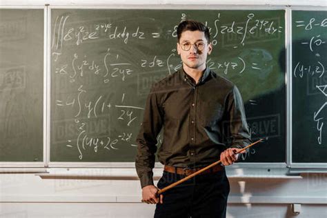 Focused Male Teacher In Formal Wear Looking At Camera And Holding Wooden Pointer In Front Of