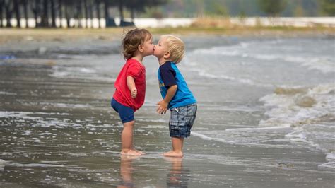 Cute Kids Are Standing On Beach Water Kissing Each Other Wearing Red