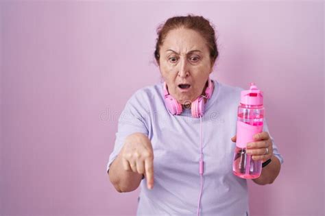 senior woman wearing sportswear and headphones pointing down with fingers showing advertisement