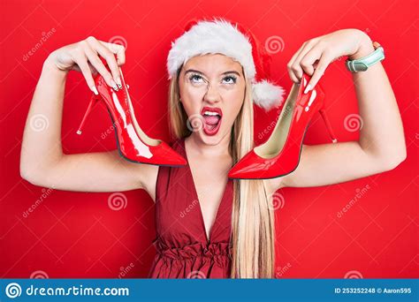 Young Blonde Girl Wearing Christmas Hat Holding High Heel Shoes Angry
