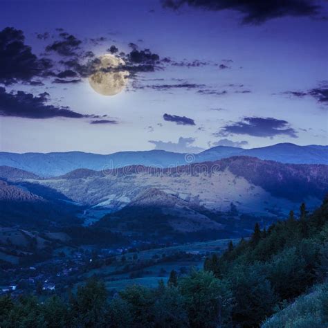 Village On Hillside Meadow With Forest In Mountain At Night Stock Photo