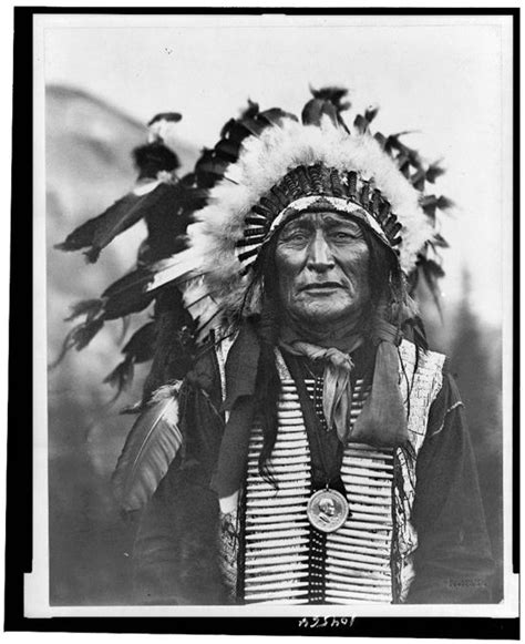 an old black and white photo of a native american man with feathers on his head