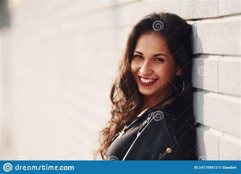 potrait of cheerful brunette with curly hair and in black clothes leaning on the wall stock