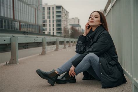 Fashionable Relaxed Young Woman Sitting On Sidewalk Near Road Urban