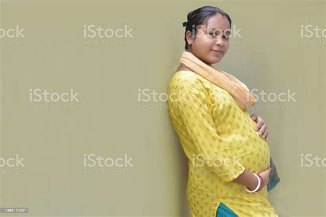 a pregnant indian lady with yellow dress and hands on belly motherhood and pregnancy concept