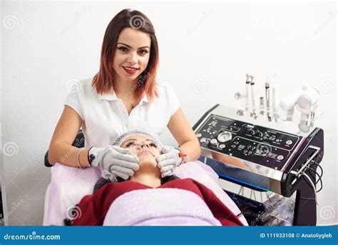 Woman Cosmetologist Is Giving Facial Massage To A Female Patient In A Beauty Salon Cosmetology