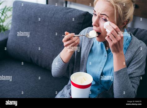 Woman Eating Ice Cream And Crying While Siitng On Couch At Home Alone