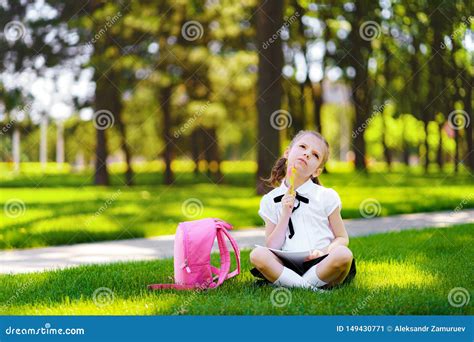 Little School Girl With Pink Backpack Sitting On Grass After Lessons