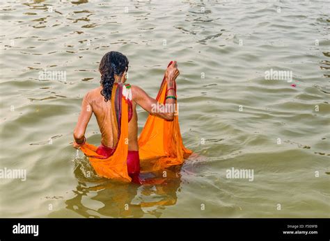Woman In Orange Sari Taking Bath In The Water Of River Ganges Early Morning At The Sangam The