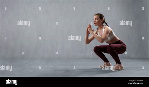 sports woman in fashion sport clothes squatting doing sit ups in gym over gray background stock