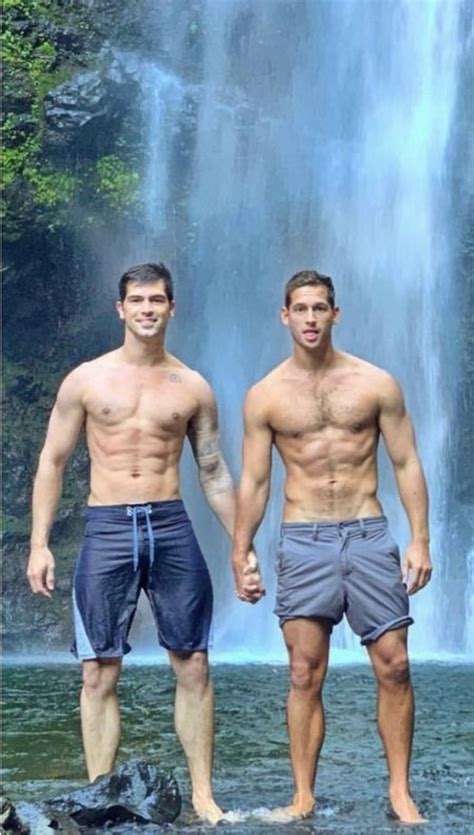 Two Men Standing In Front Of A Waterfall With No Shirts On And One Man Without His Shirt