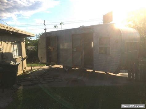 An Old Trailer Is Parked In The Back Yard Near A House With A Sun