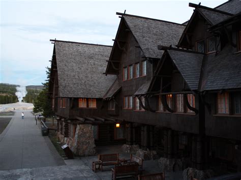 A crowd on the porch of the old faithful inn watches old faithful geyser erupt. Old Faithful Inn hotel in Yellowstone National Park ...