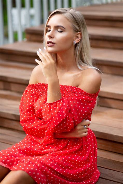 Tender Blonde Model With Naked Shoulders Wearing Red Dress Posing On The Wooden Staircase Stock