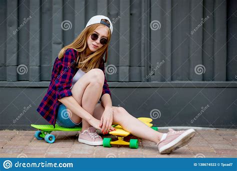 a pretty blond girl wearing sunglasses checkered shirt and denim shorts is sitting on the