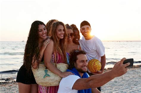 Friends Taking Selfies On A Beach At Dusk By Stocksy Contributor