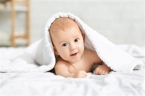 Adorable Smiling Baby Boy Lying On Bed Under White Blanket Stock Image