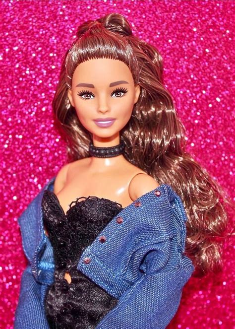 a close up of a barbie doll wearing a black dress and blue denim jacket with pink glitter behind her