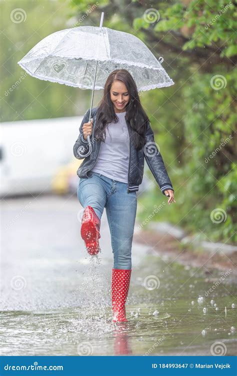 Woman With An Umbrella Walking In Rainboots In A Puddle Under A Heavy