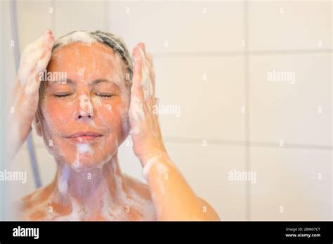 Blissful Middle Aged Woman Enjoying A Shower Soaping Her Face With Her Hands To Her Cheeks And