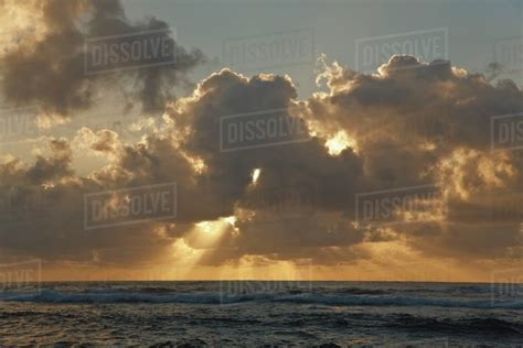 Sun Rays Spread From Clouds At Sunrise Over The Ocean Stock Photo