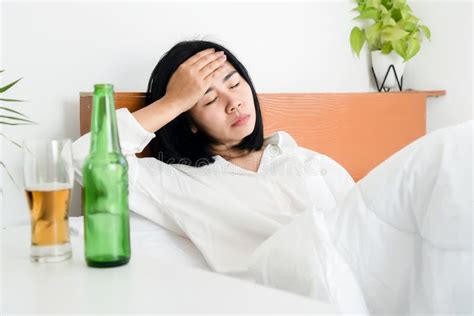 asian woman hangover and having a headache after drinking beer wakeup in morning lying down in