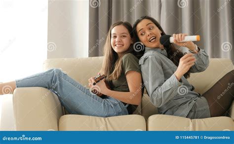 Two Sisters Having Fun On The Couch One Is Playing At Ukulele And The