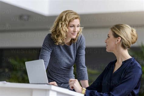 Two Women Talking At Desk In Office Stock Photo