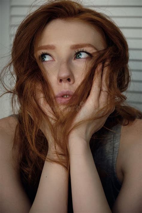 Headshot Red Haired Girl With Freckles Looks Away Putting Her Chin In Open Hands Against A