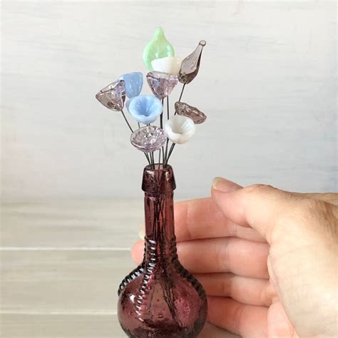 A Hand Holding A Small Glass Vase With Flowers In It