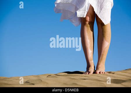 A Girl With Sand Covered Bare Feet Sits On The Beach Stock Photo