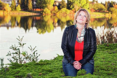 mature christian woman kneeling and praying beside lake in autumn edmonton alberta canada
