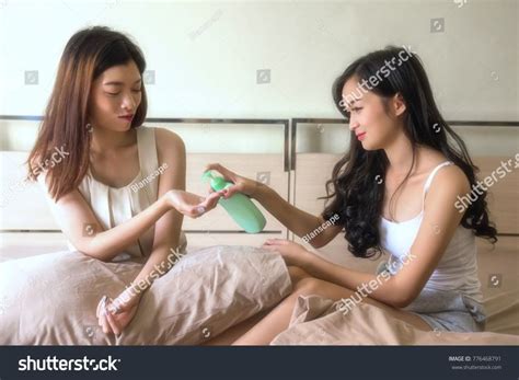 Asian Beautiful Woman Give Moisture Cream Lotion To Her Cute Friend Or Roommate On The Bed Two
