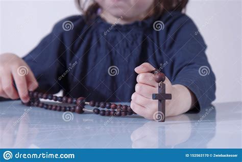 Little Child Girl Praying And Holding A Wooden Rosary As