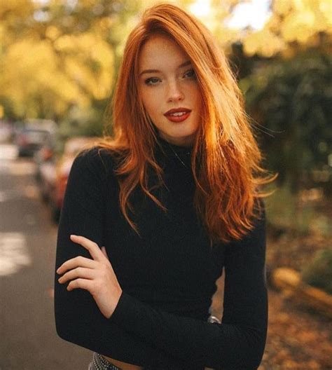 A Woman With Long Red Hair Is Posing For The Camera While Wearing A Black Turtle Neck Sweater