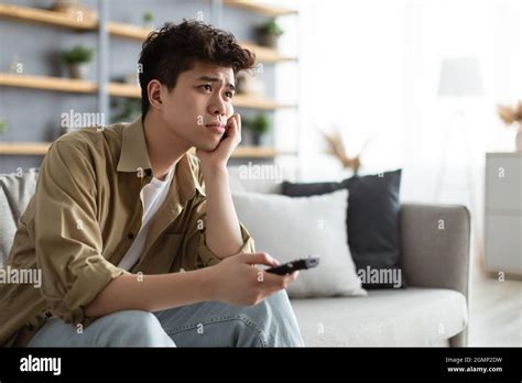 Bored Asian Man Watching Television Sitting On Couch Stock Photo Alamy