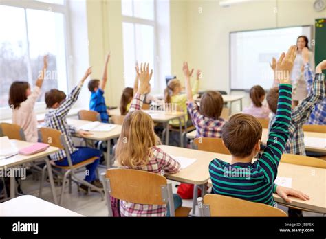 Group Of School Kids Raising Hands In Classroom Stock Photo Alamy