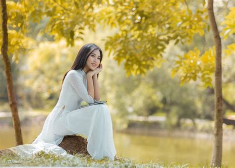 A Woman In White Dress Sitting On Rock Next To Water And Trees With Yellow Leaves
