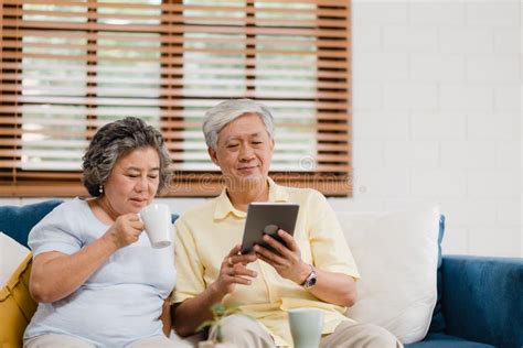 Asian Elderly Couple Using Tablet And Drinking Coffee In Living Room At