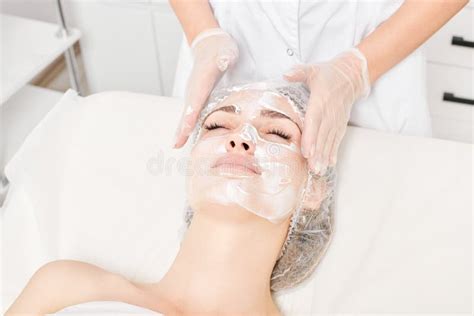 Cosmetologist Massages Cream Mask Into Woman Face Skin For Rejuvenation Procedure In Beauty