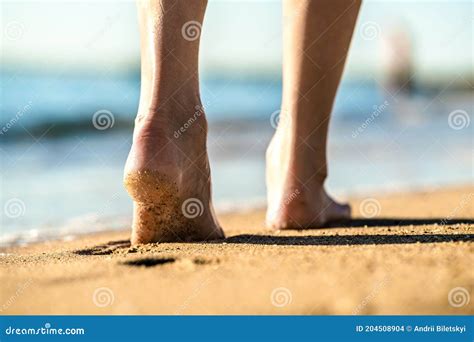 close up of woman feet walking barefoot on sand leaving footprints on golden beach vacation