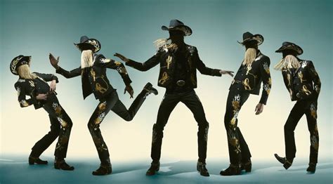 Four People Dressed In Black And Gold Are Dancing With Hats On Their Heads Arms And Legs