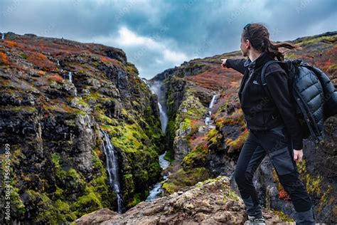 Youn Woman Pointing On Glymur Waterfall Canyon On The Cliffs In Iceland