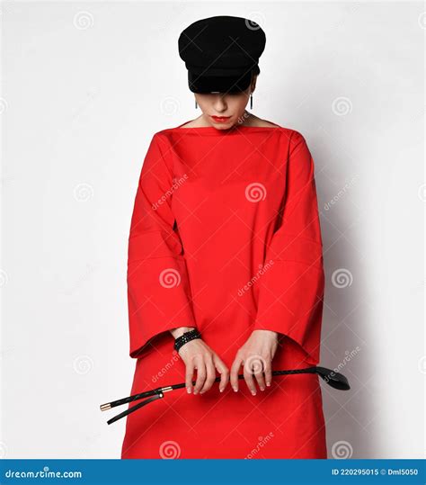 Short Haired Brunette Woman In Red Casual Dress And Hat Standing Holding Whip In Hands Looking