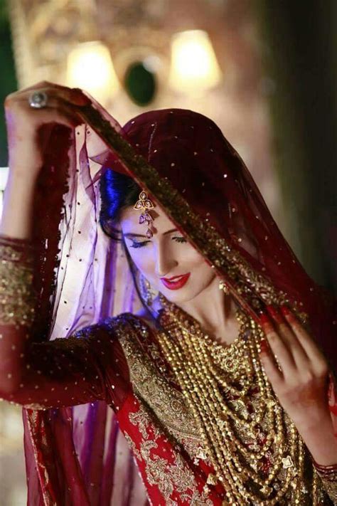 a woman in a red and gold bridal outfit is holding her veil over her head