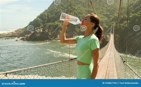 Sport Girl Drinking Water On A Bridge Near The Ocean After Jogging